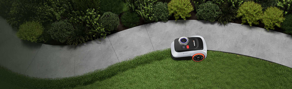 Navimow i105E Mähroboter mäht den Rasen neben dem grauen Gartenweg.